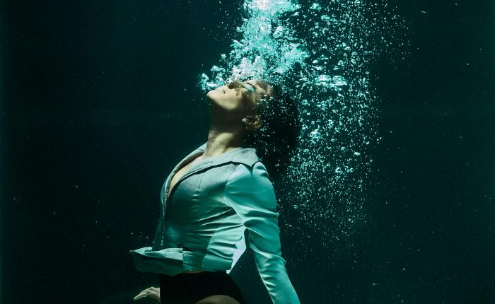 Dramatic photo of a woman diving underwater in stylish attire.